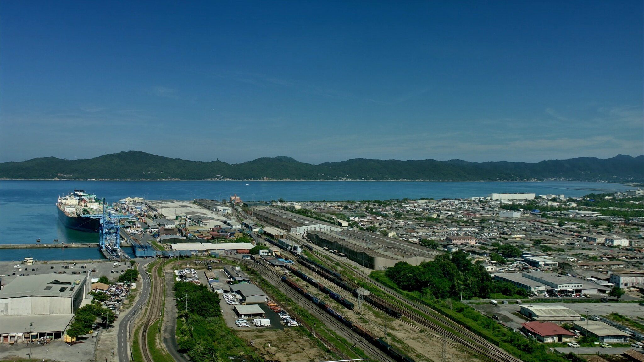Complexo de porto, ferrovia e distrito industrial no litoral, visto do alto em um dia de sol