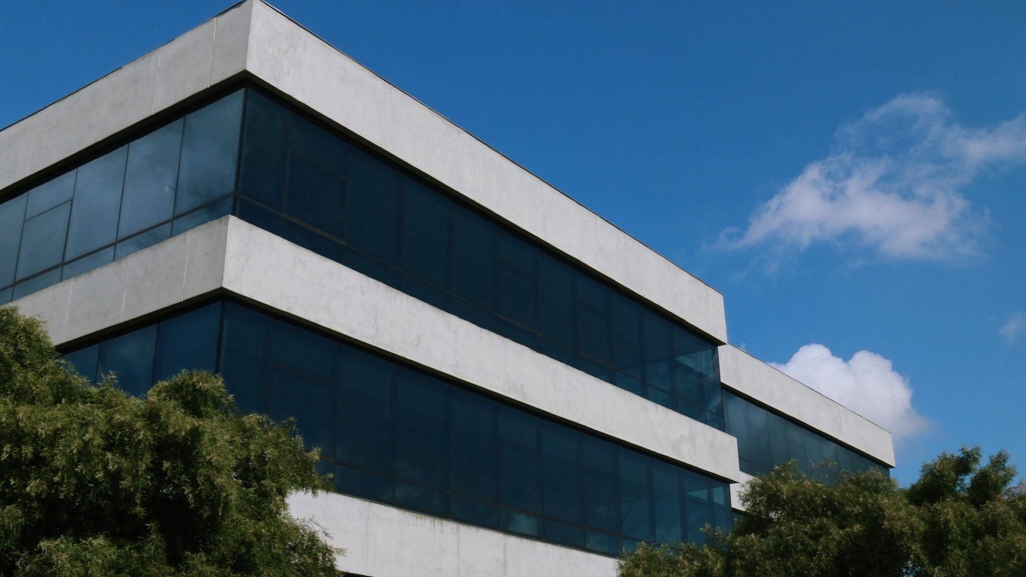 Fachada de concreto e vidro refletindo um céu azul com nuvens