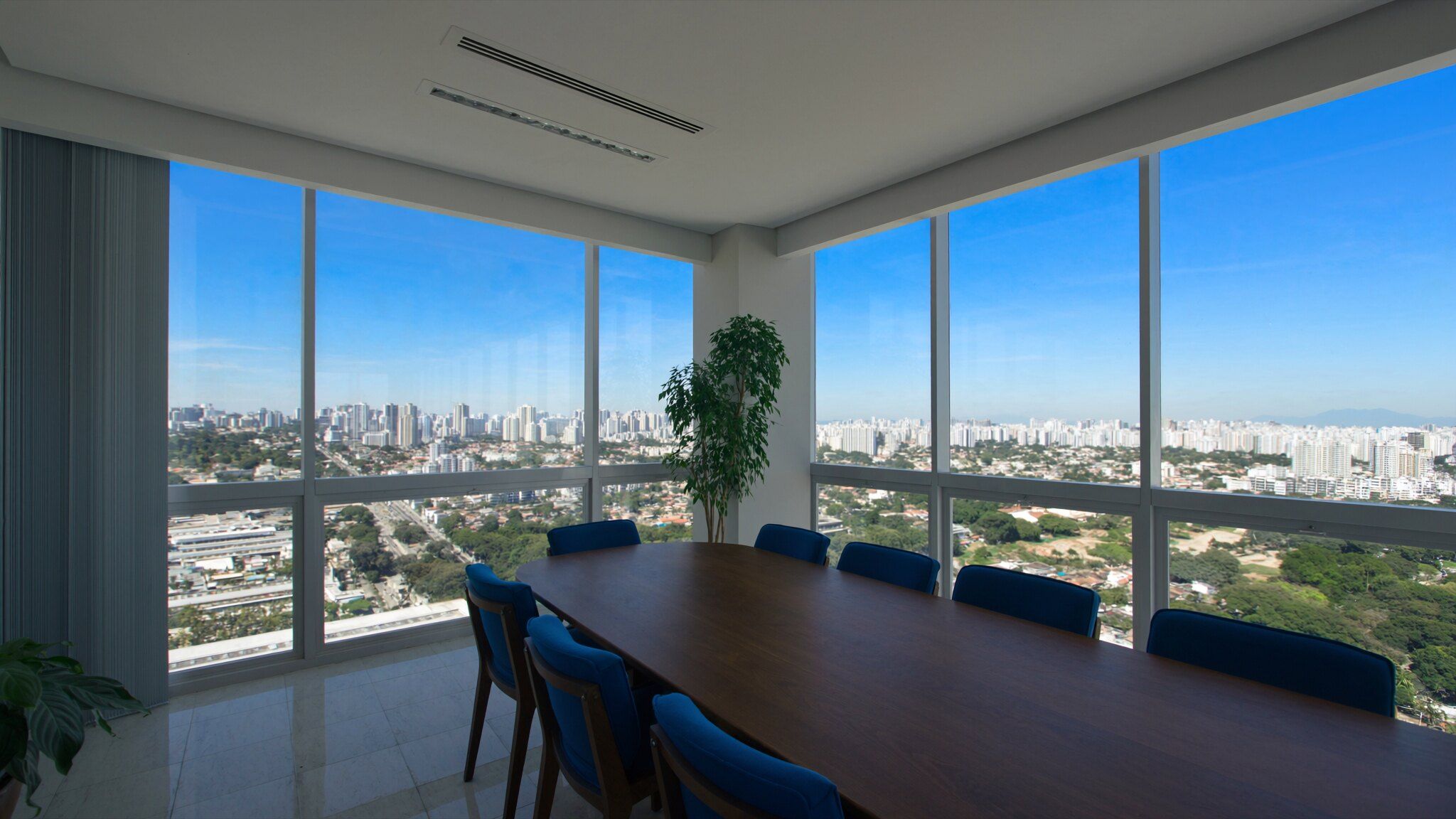 Sala de reunião vazia, com cadeiras azul-marinho e janelas amplas para a cidade em um dia de sol
