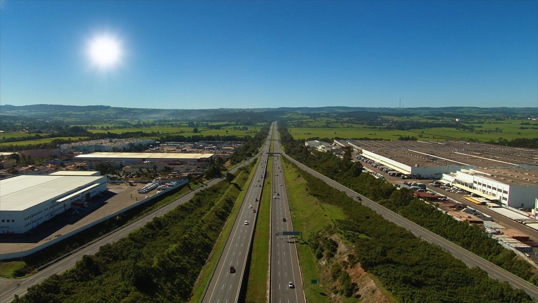 Corredor industrial e logístico ao longo de uma rodovia, visto do alto em um dia de sol
