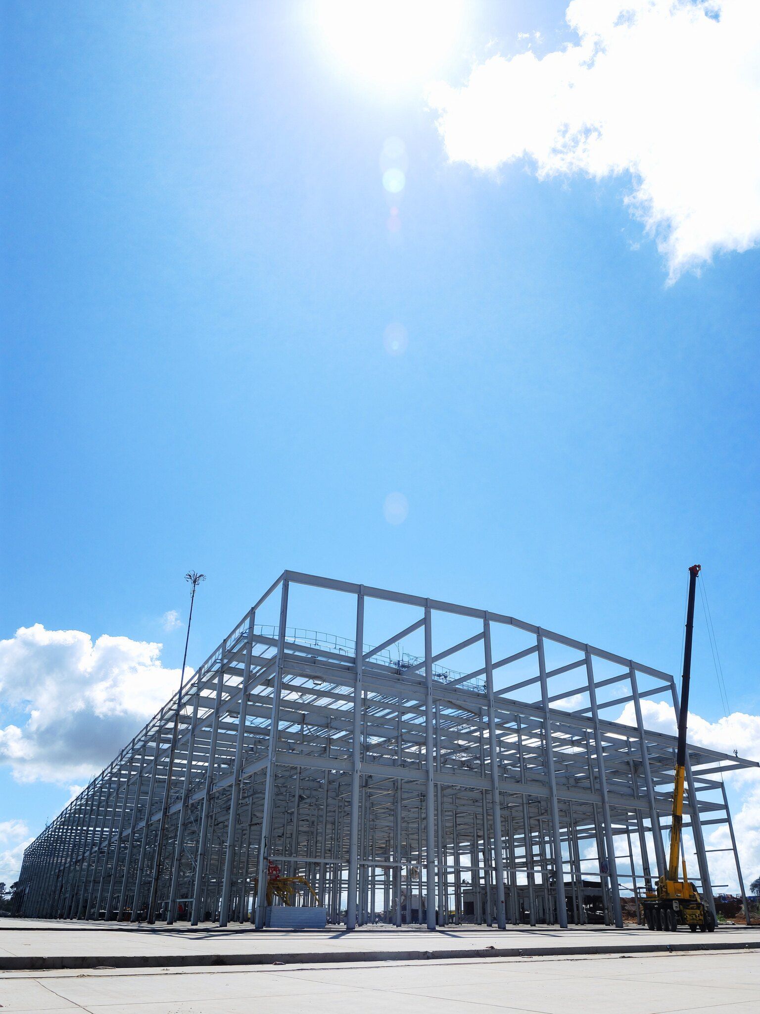 Estrutura metálica de uma planta industrial em obra, com um guindaste ao lado, em um dia de sol