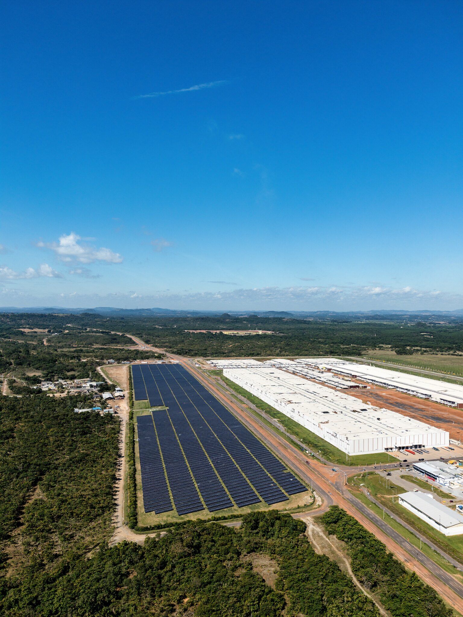 Usina solar e centro logístico vistos do alto em um dia de sol