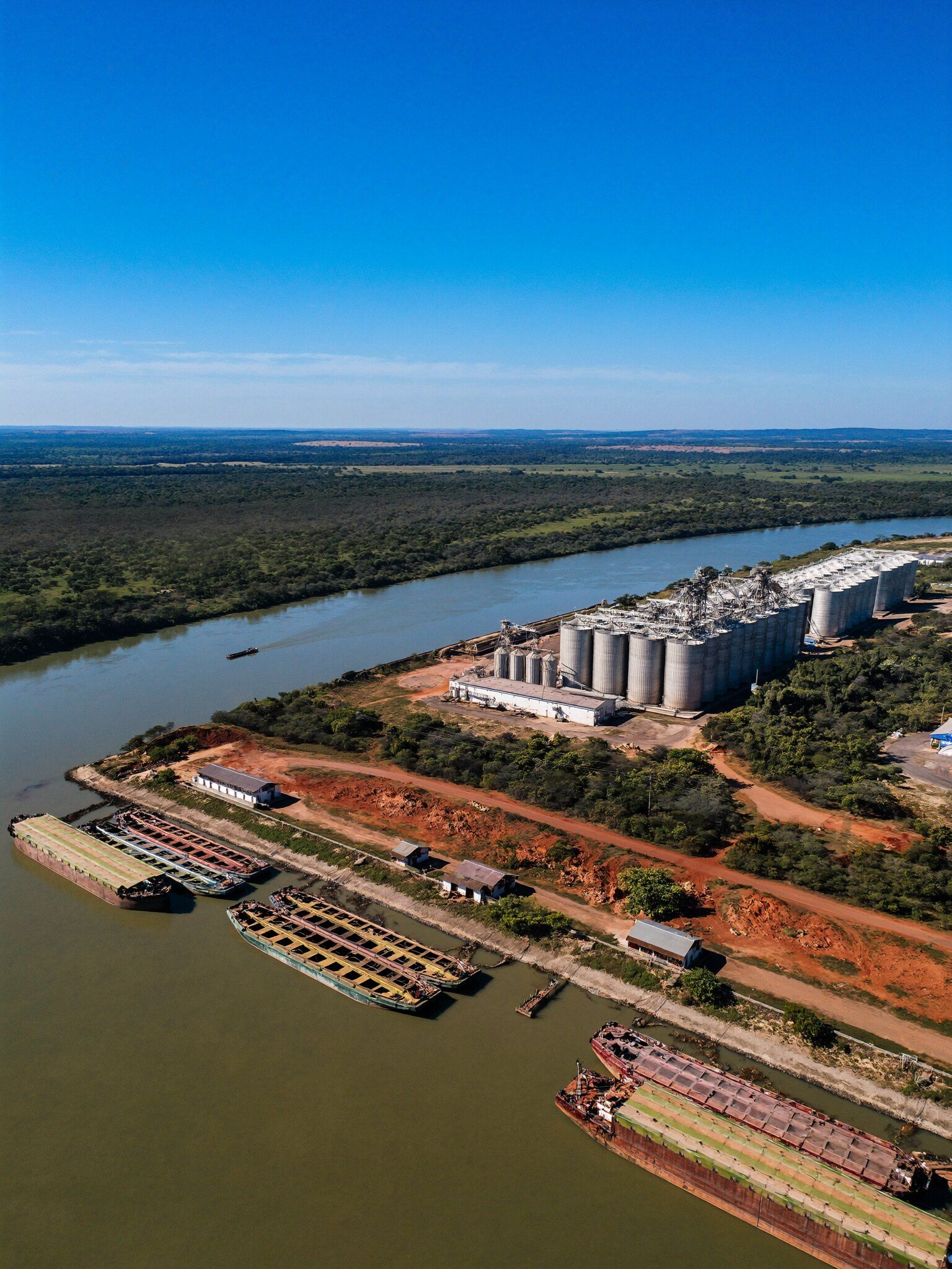 Porto fluvial com silos e barcaças, ligado por estradas de terra vermelha no cerrado