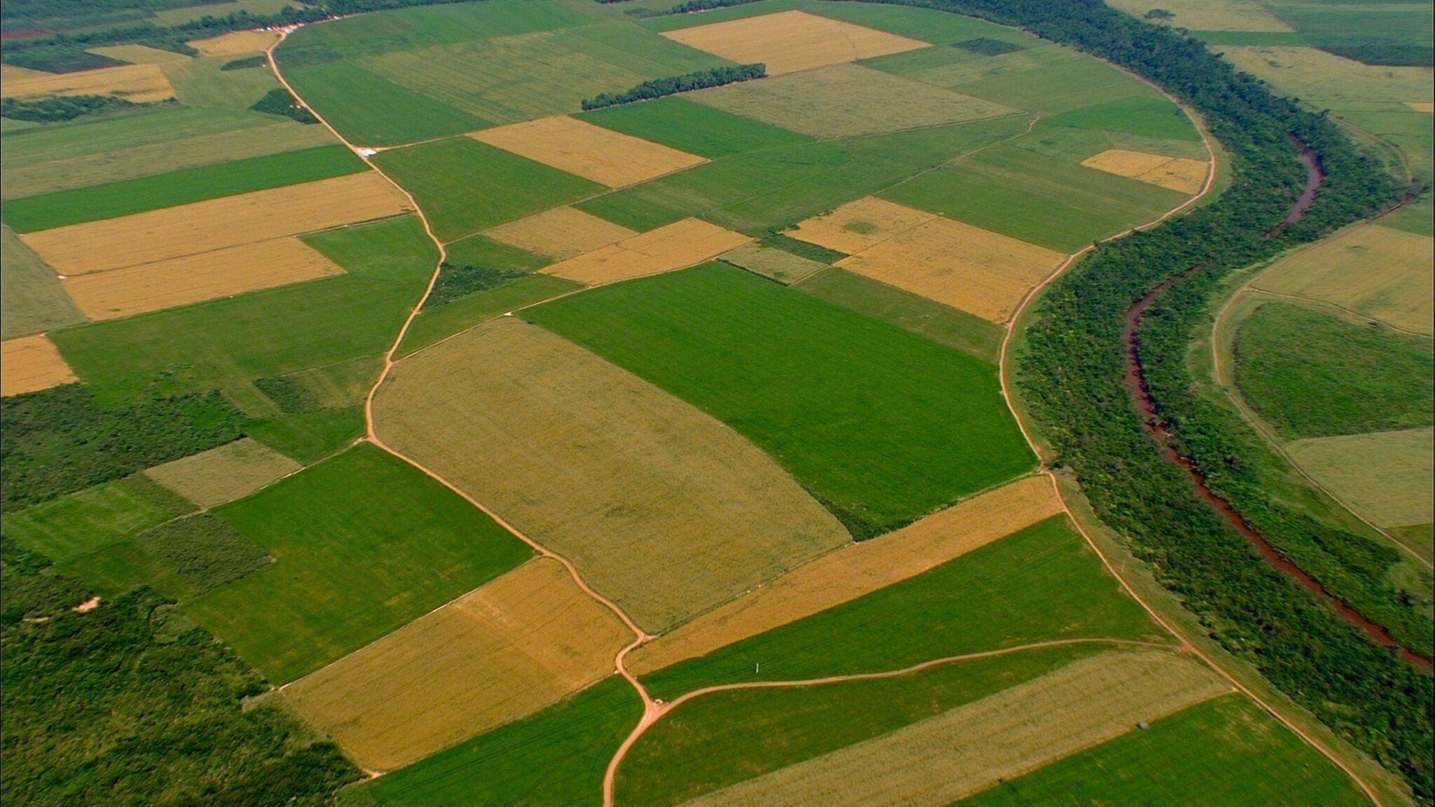Mosaico de lavouras, estradas e um rio margeado de mata no Brasil central, visto do alto