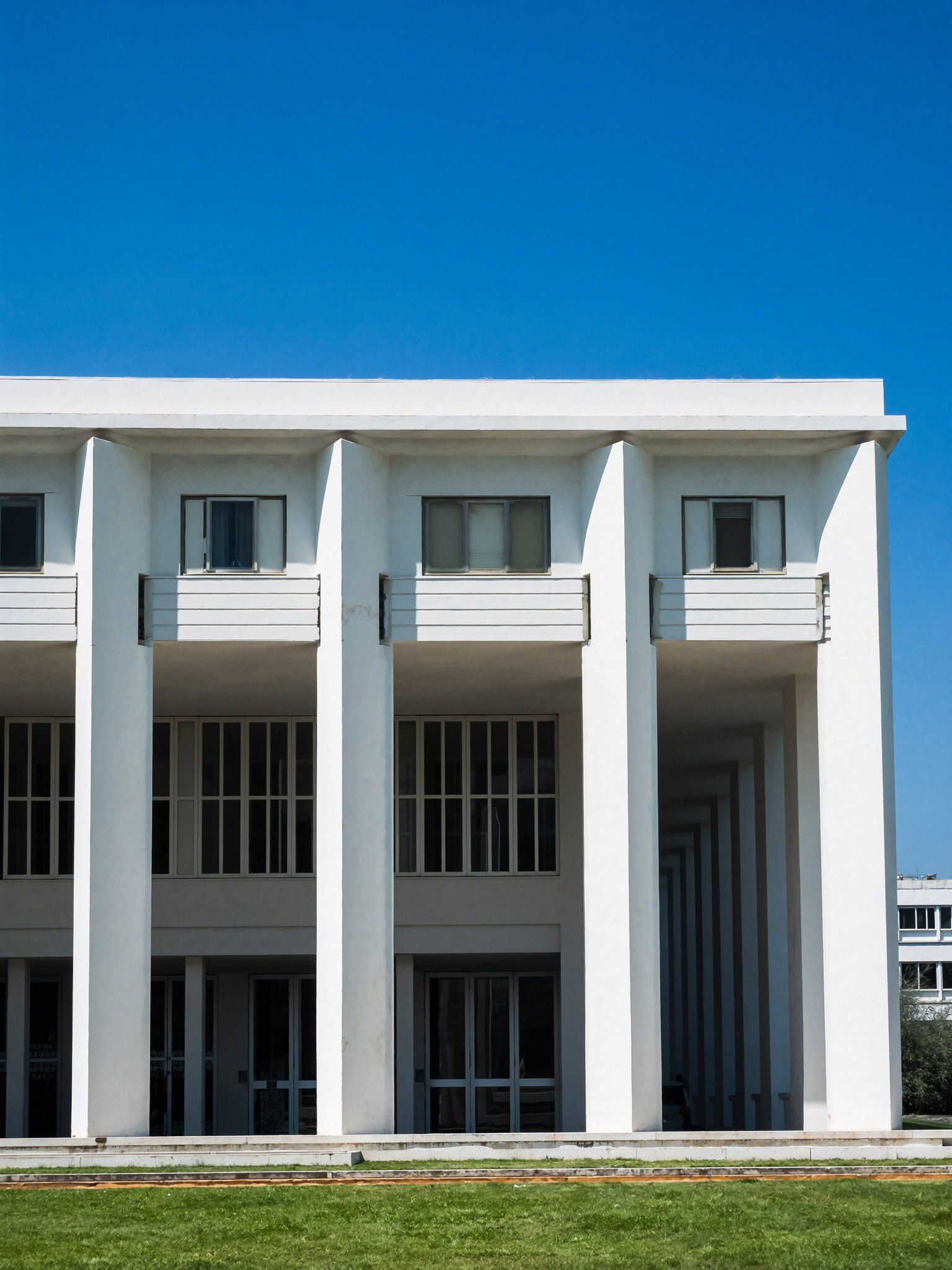 Fachada de edifício institucional modernista com colunas brancas, sob céu azul