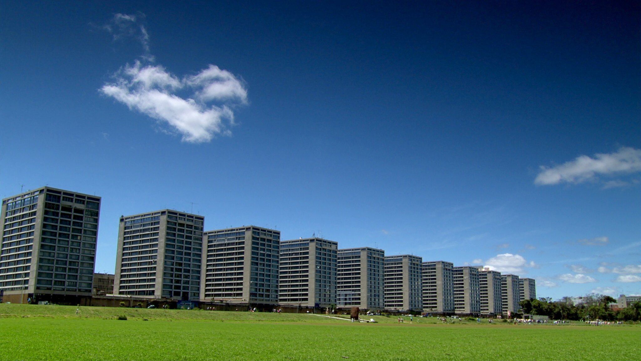 Edifícios modernistas em fila sobre um gramado amplo, sob céu azul